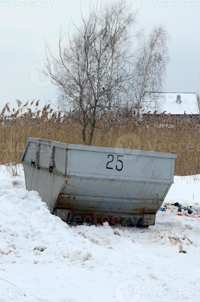 Trash bin at the side of street in winter with lip garbage container winter snow. Metal container for household waste photo