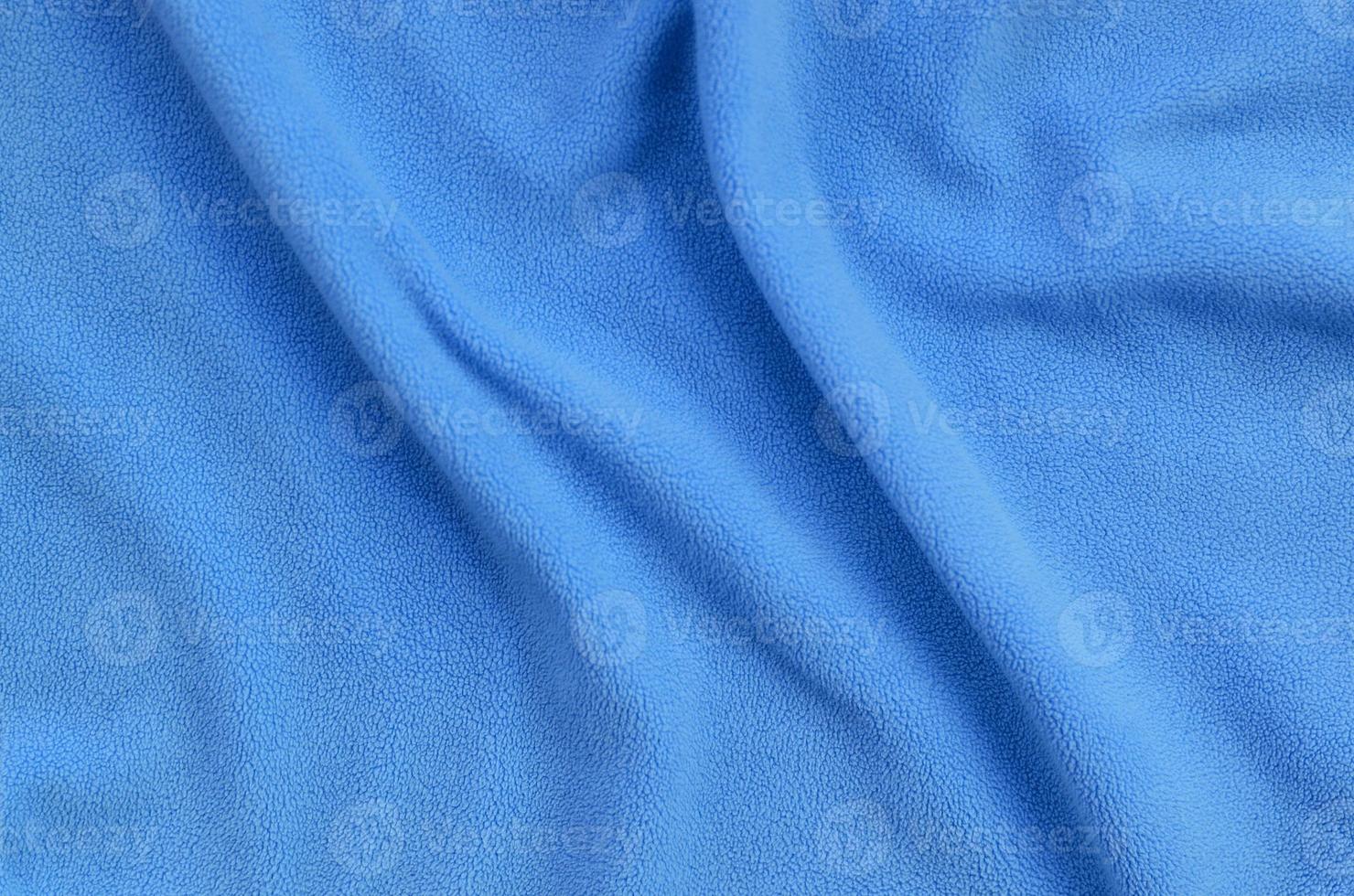 The blanket of furry blue fleece fabric. A background of light blue soft plush fleece material with a lot of relief folds photo