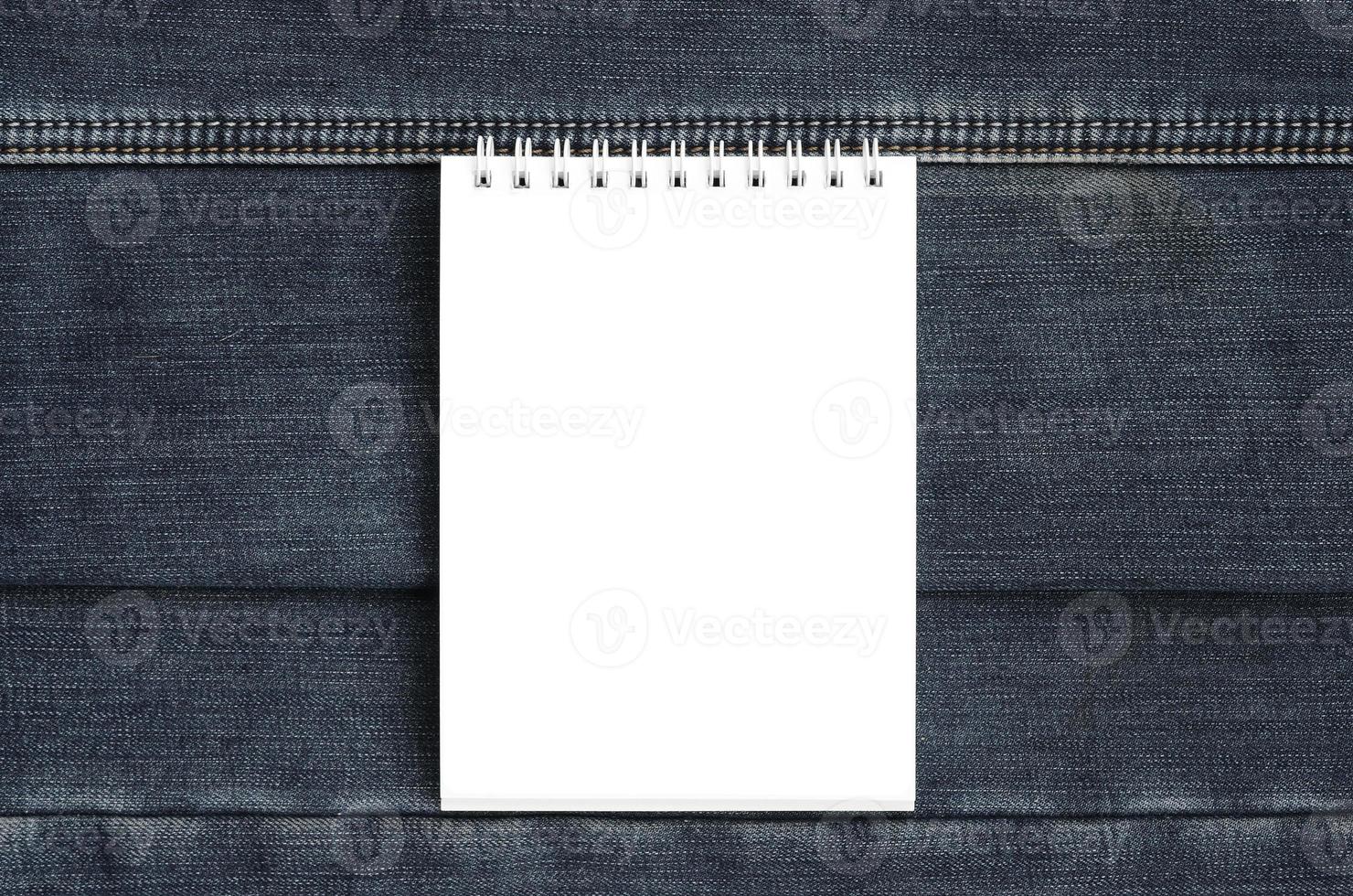 White notebook with clean pages lying on dark blue jeans background. Image with copy space photo