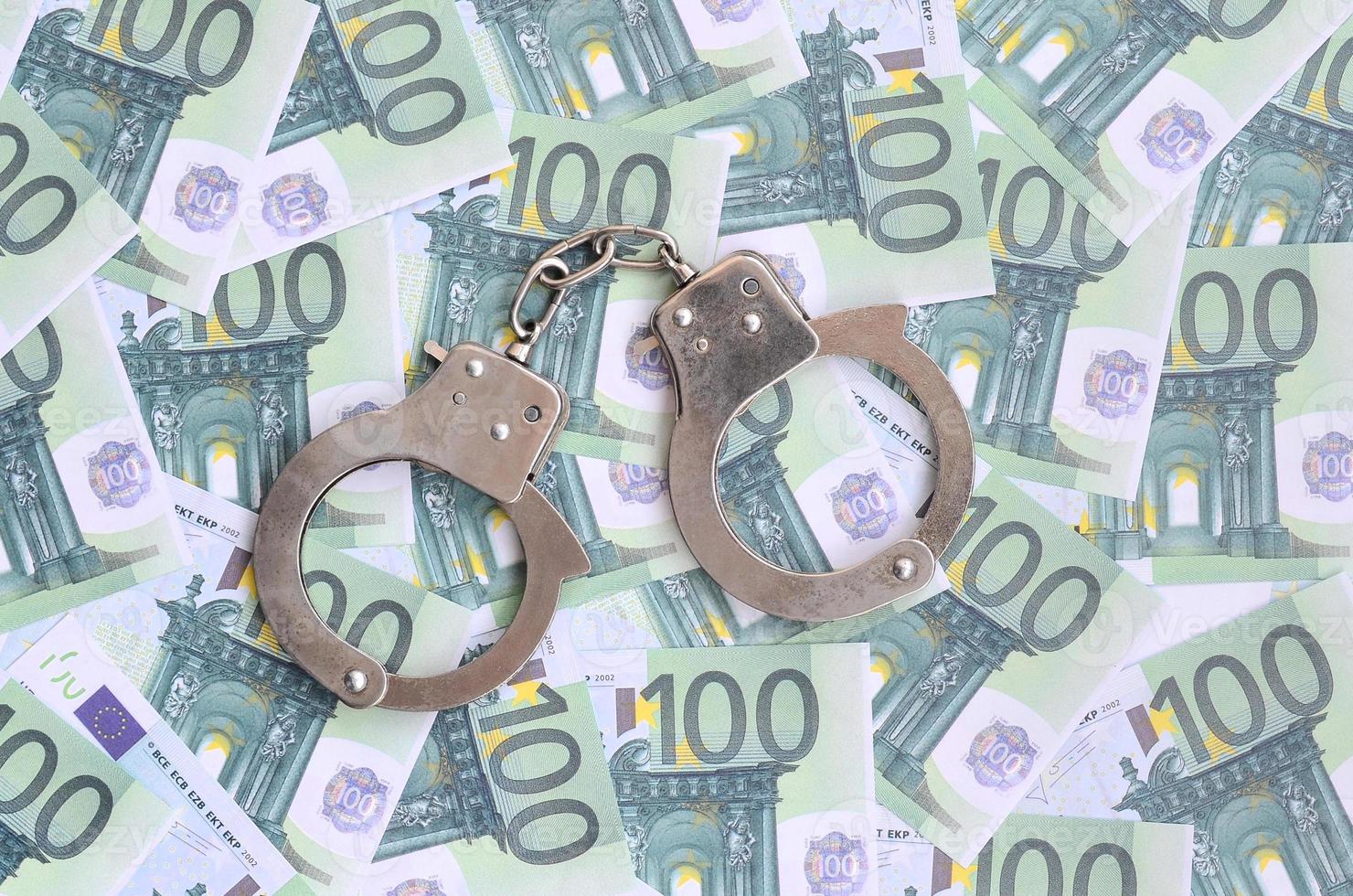 Police handcuffs lies on a set of green monetary denominations of 100 euros. A lot of money forms an infinite heap photo