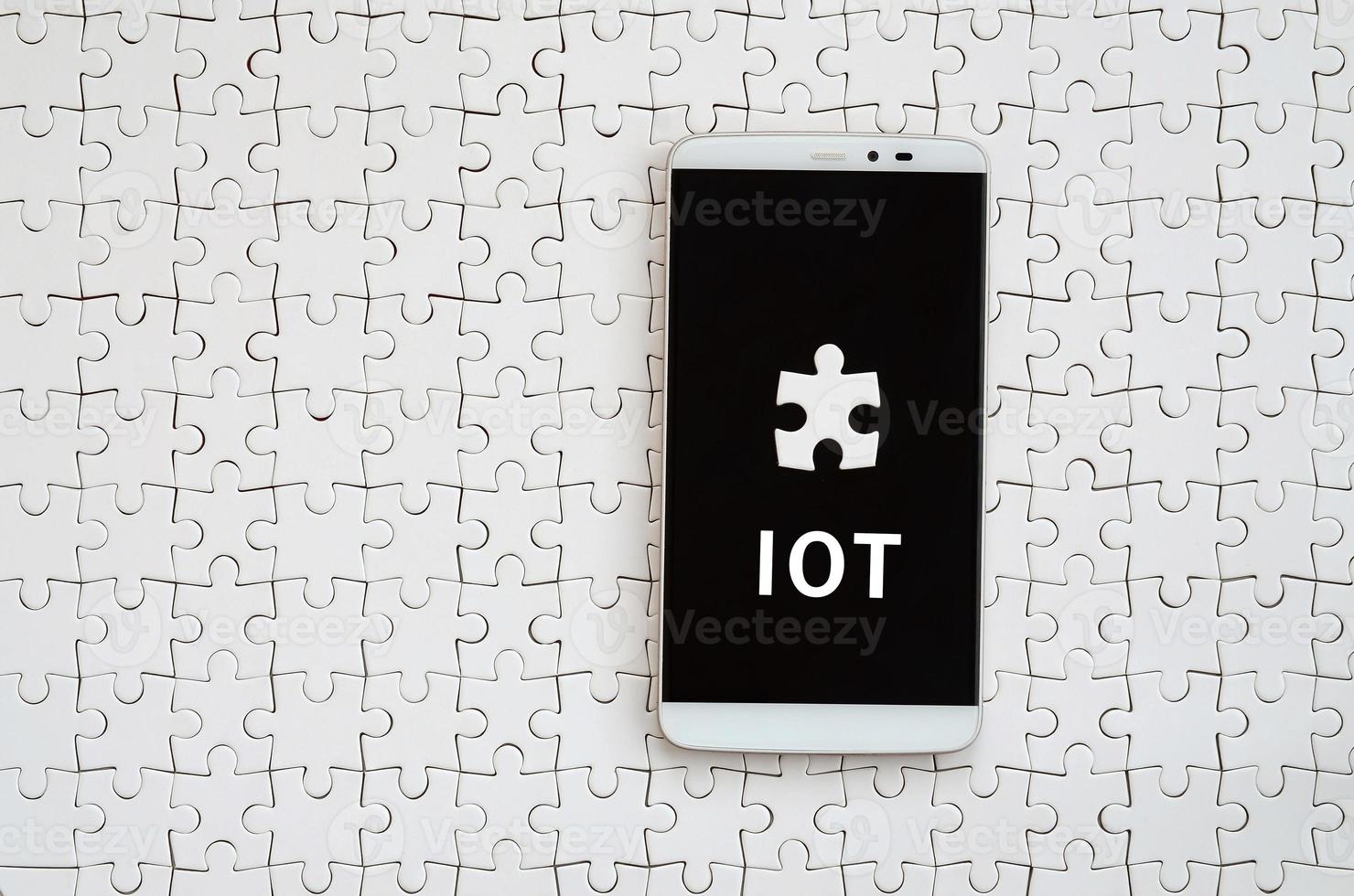 A modern big smartphone with a touch screen lies on a white jigsaw puzzle in an assembled state with inscription. IOT photo