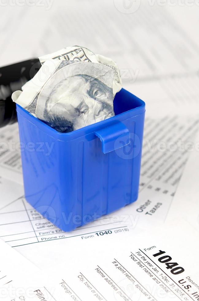 Many american tax blank forms and crumpled hundred dollar bill in trash bin photo