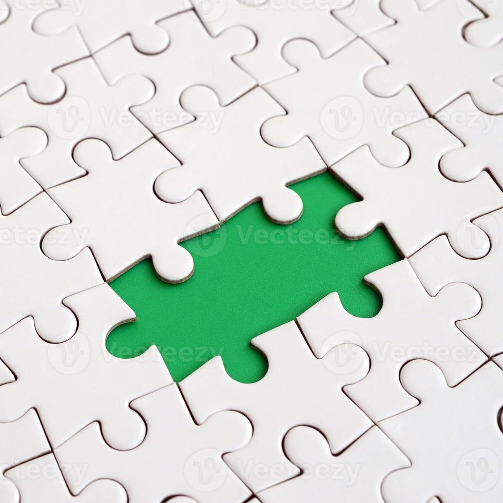 Close-up texture of a white jigsaw puzzle in assembled state with missing elements forming a green pad for text. Copy space photo