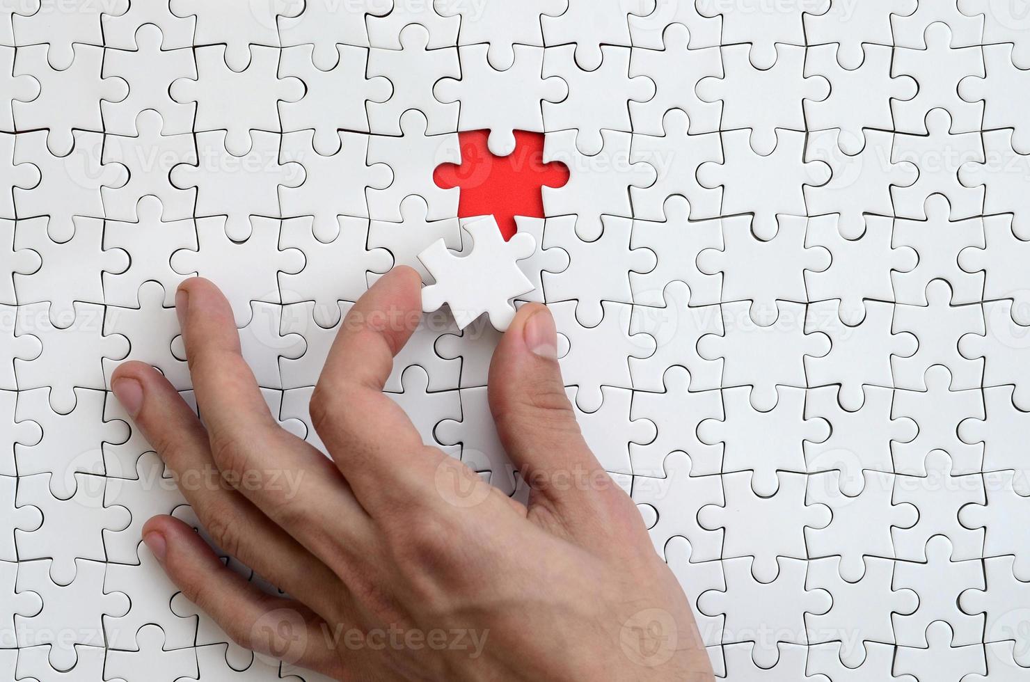 The texture of a white puzzle puzzle in the assembled state with one missing element that the male hand puts in photo