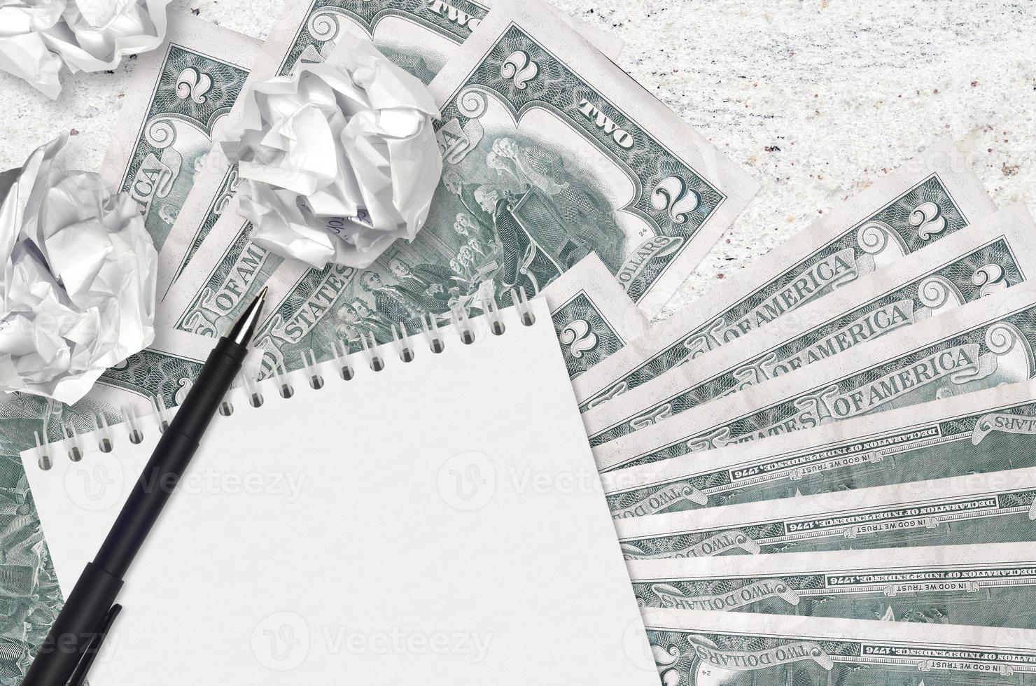 2 US dollars bills and balls of crumpled paper with blank notepad. Bad ideas or less of inspiration concept. Searching ideas for investment photo