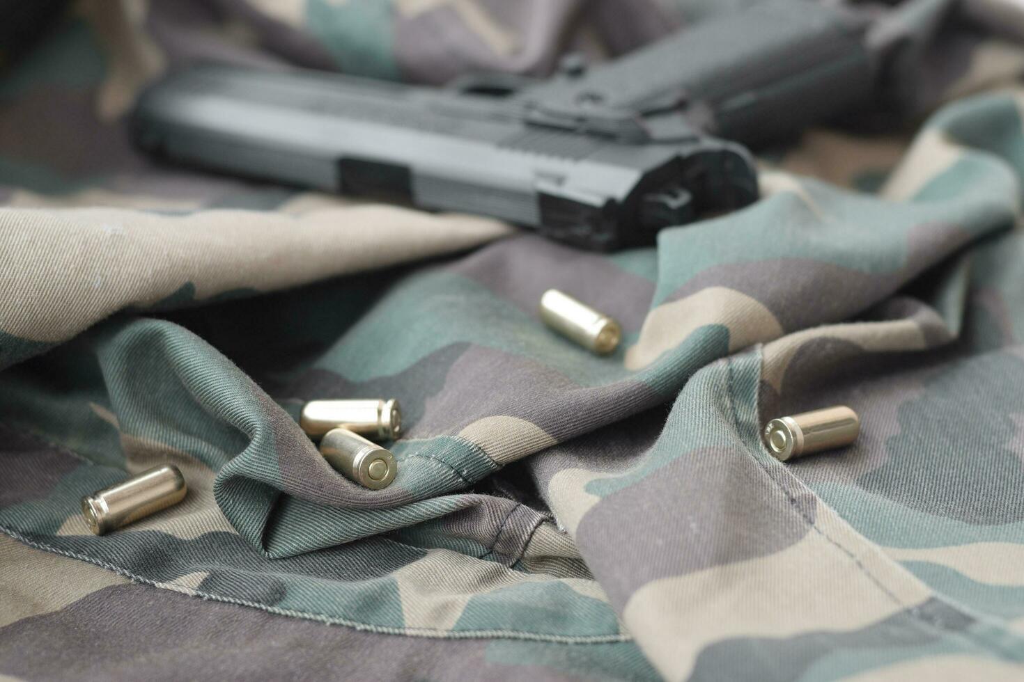9mm bullets and pistol lie on folded camouflage green fabric. A set shooting range items or a self-defense kit photo
