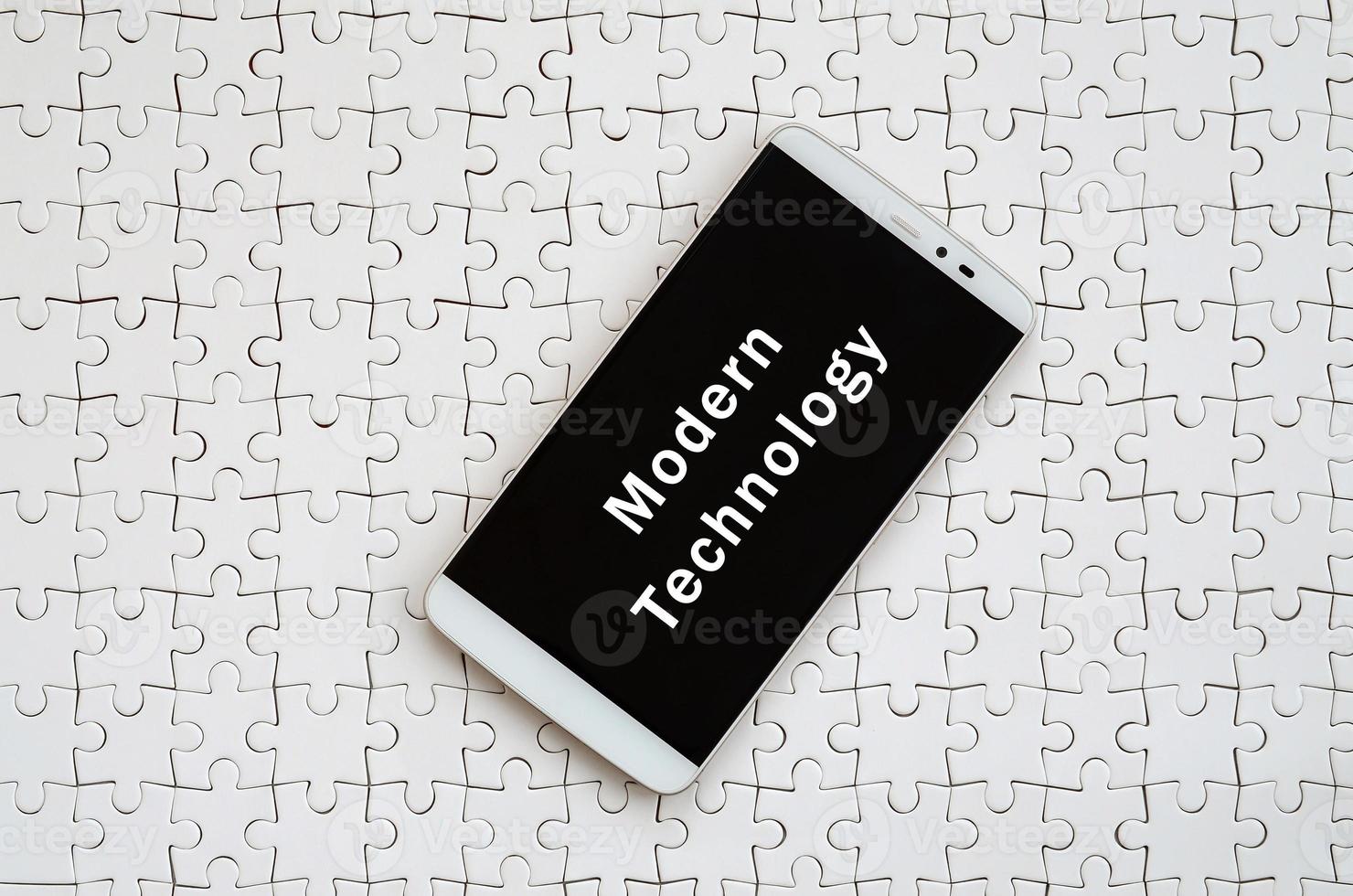 A modern big smartphone with a touch screen lies on a white jigsaw puzzle in an assembled state with inscription. Modern technology photo