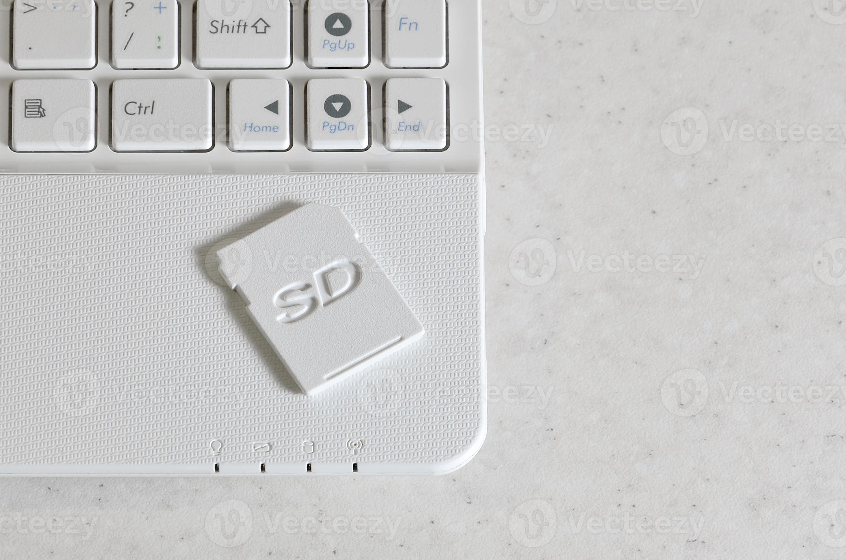 A compact SD memory card lies on a white netbook. The digital