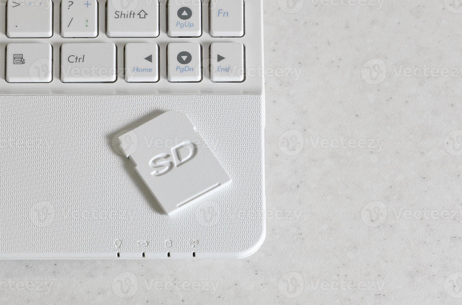 A compact SD memory card lies on a white netbook. The digital information storage device is ready for use. Concept of modern technologies photo