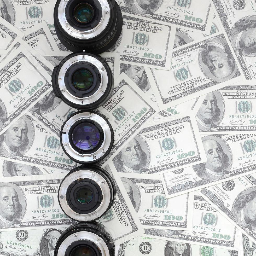 A few photographic lenses lies on the background of a lot of dollar bills. Space for text photo