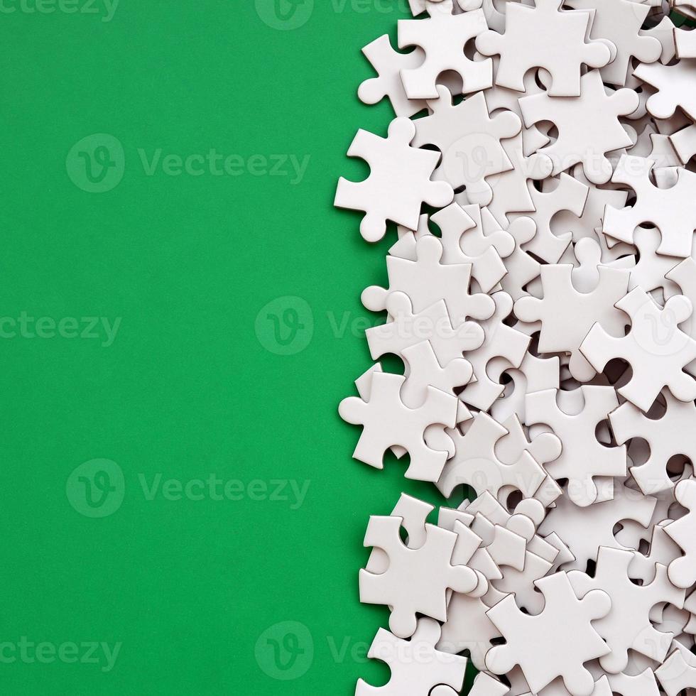 A pile of uncombed elements of a white jigsaw puzzle lies on the background of a green surface. Texture photo with copy space for text