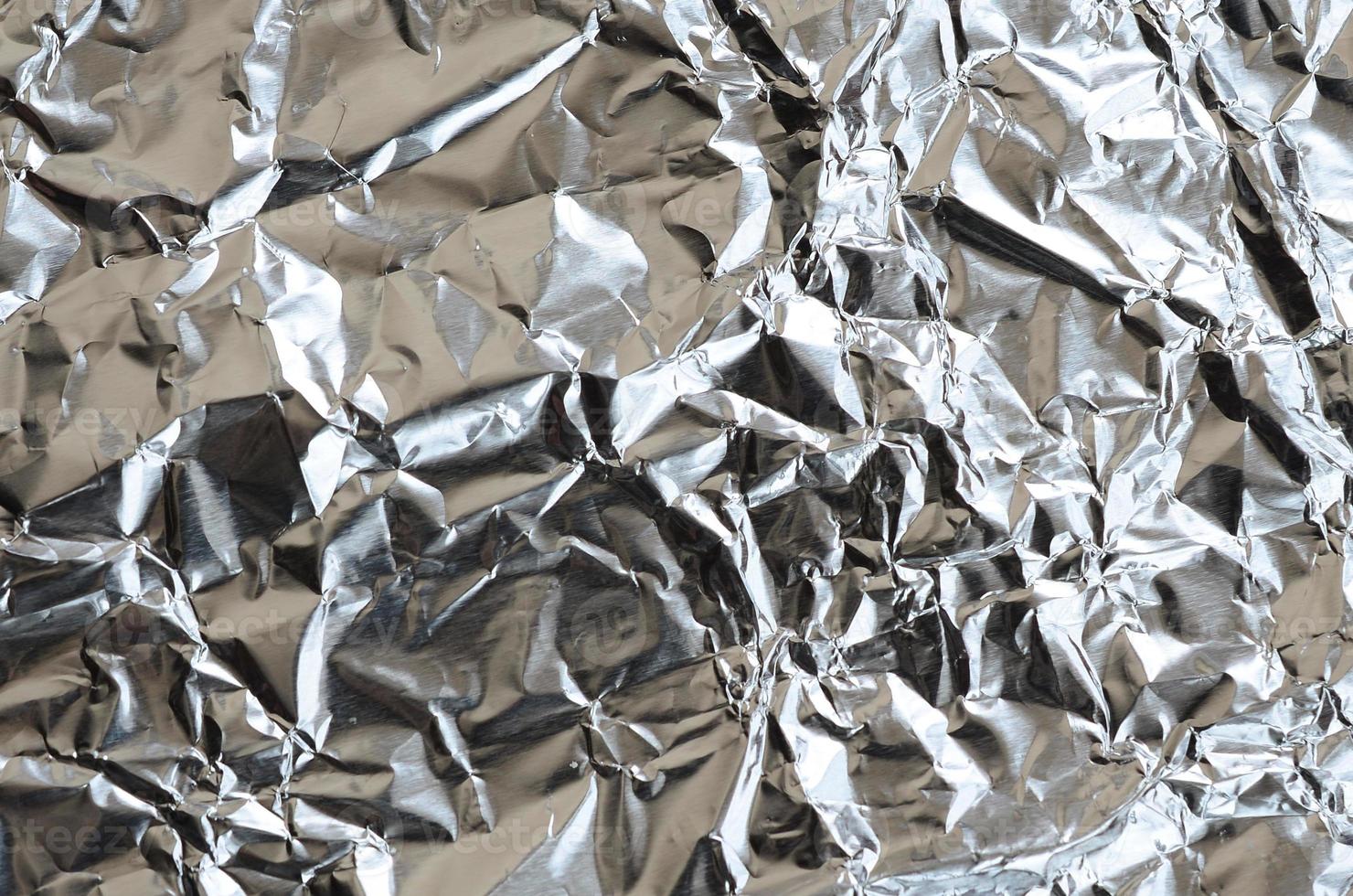 Thin wrinkled sheet of crushed tin aluminum silver foil background with shiny crumpled surface for texture photo