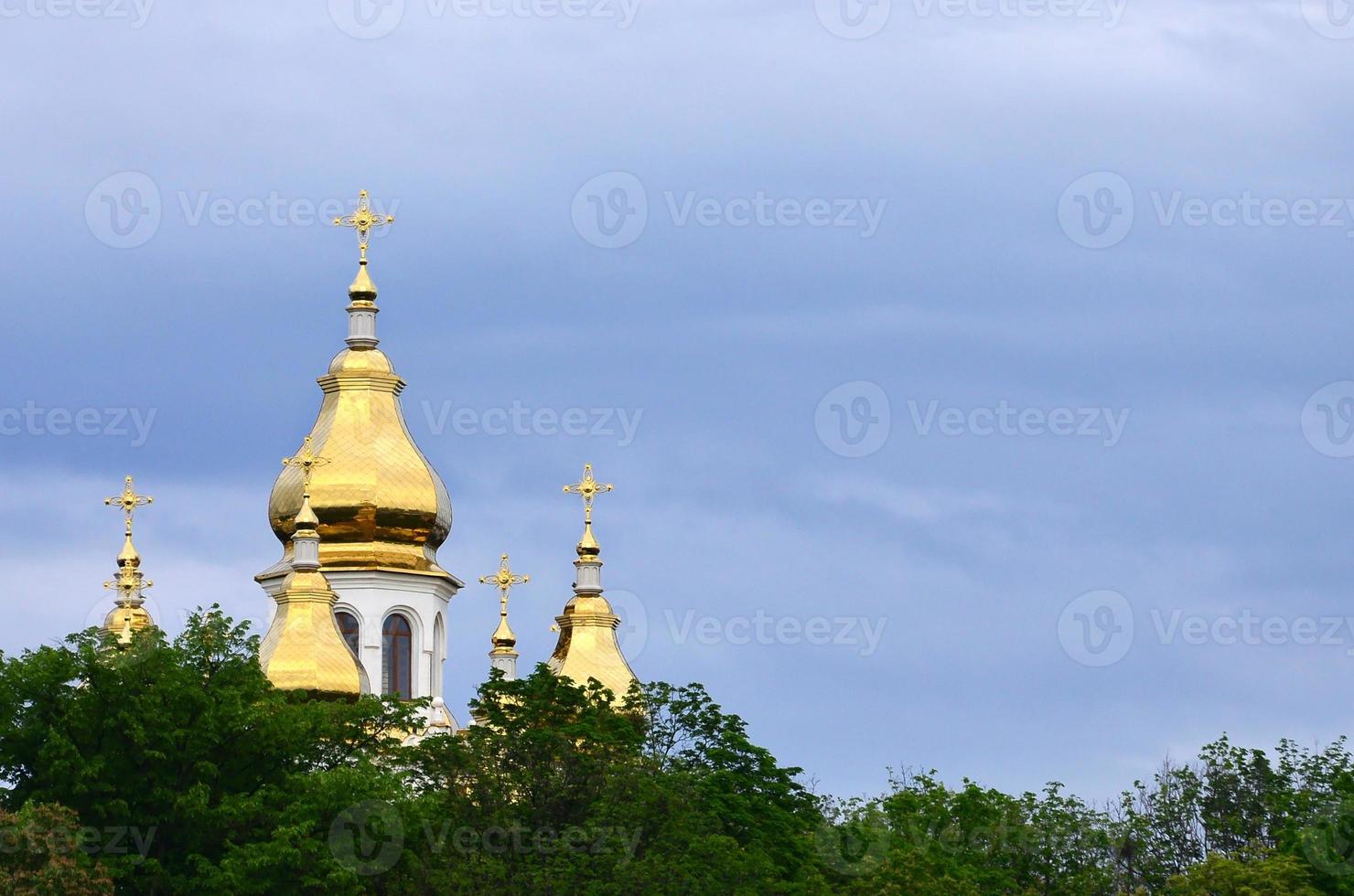 cúpulas doradas de una iglesia ortodoxa entre árboles florecientes sobre un fondo de cielo azul nublado foto