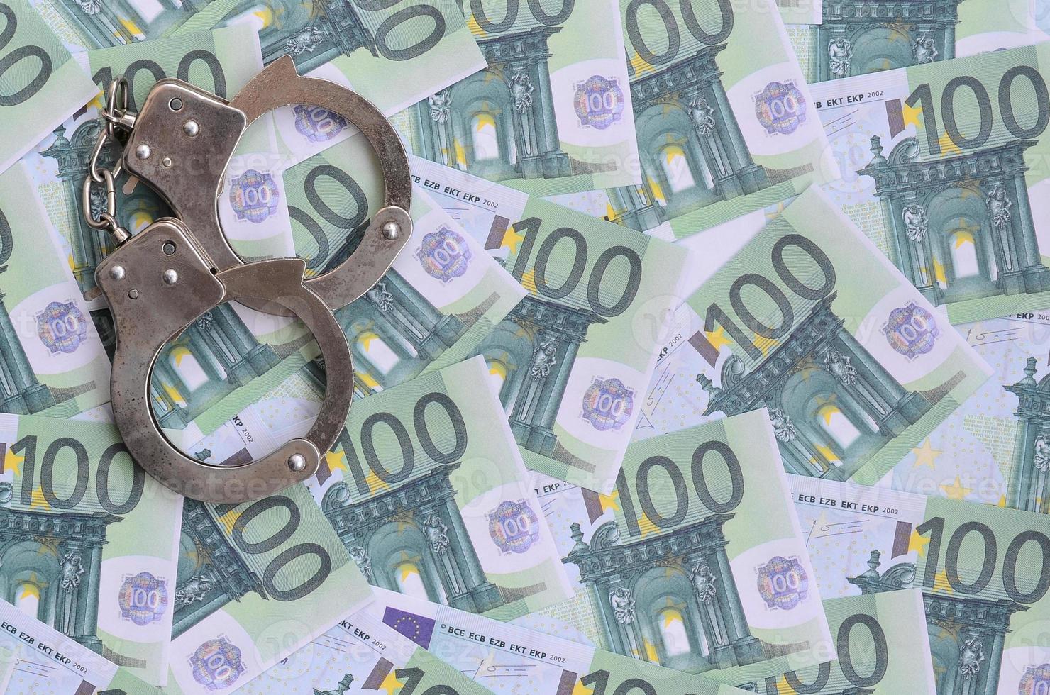 Police handcuffs lies on a set of green monetary denominations of 100 euros. A lot of money forms an infinite heap photo