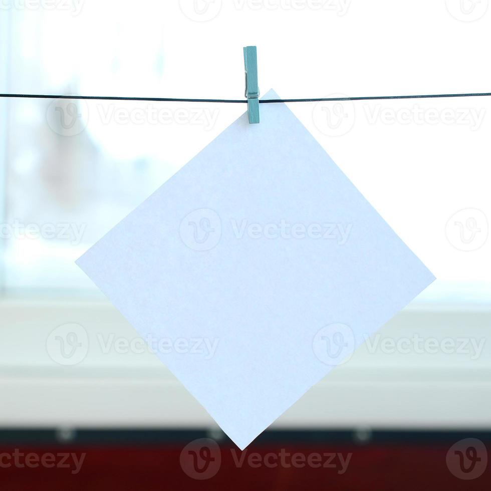 White blank card on rope, window glass background. Creative reminder, small sheet of paper on wooden clothespin, memo backdrop photo