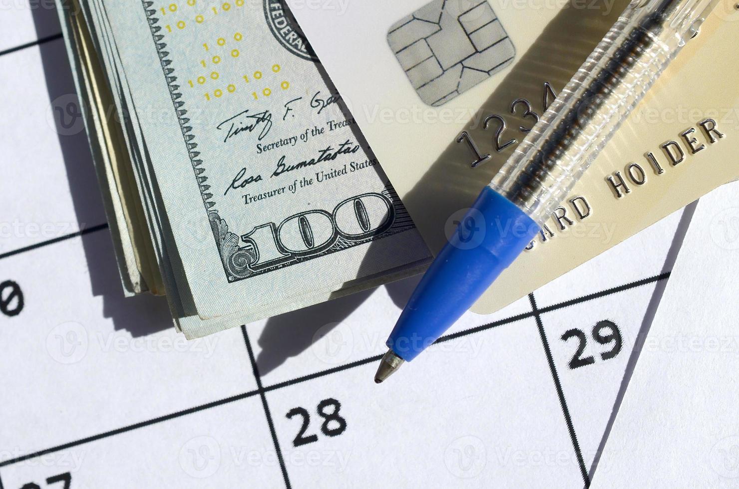 Pen and credit card on many hundred US dollar bills on calendar page close up photo