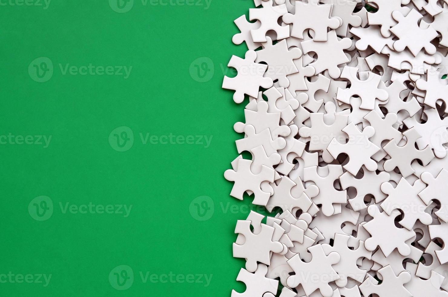 A pile of uncombed elements of a white jigsaw puzzle lies on the background of a green surface. Texture photo with copy space for text