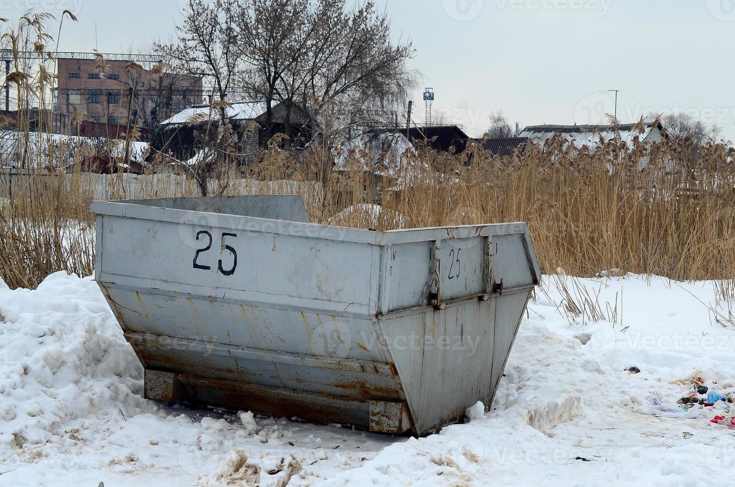 Trash bin at the side of street in winter with lip garbage container winter snow. Metal container for household waste photo