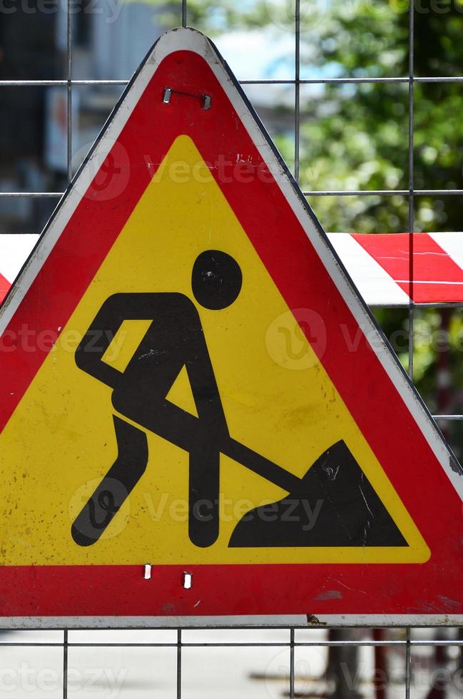 The warning sign under construction is attached to a metal mesh fence with a red and white striped signal tape photo