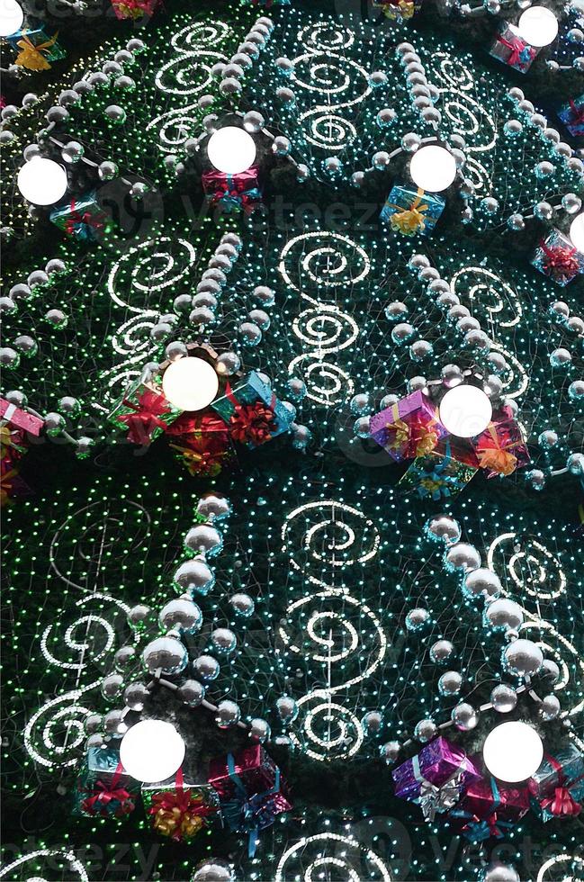 A fragment of a huge Christmas tree with many ornaments, gift boxes and luminous lamps. Photo of a decorated Christmas tree close-up