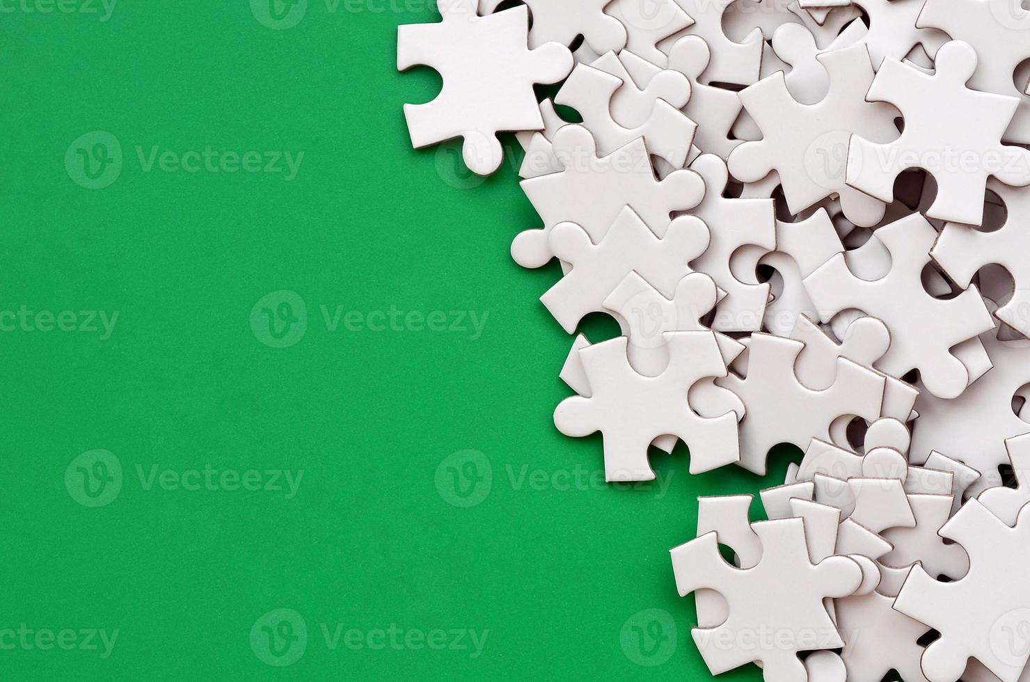 A pile of uncombed elements of a white jigsaw puzzle lies on the background of a green surface. Texture photo with copy space for text