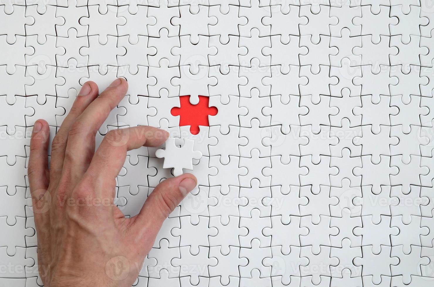 The texture of a white puzzle puzzle in the assembled state with one missing element that the male hand puts in photo