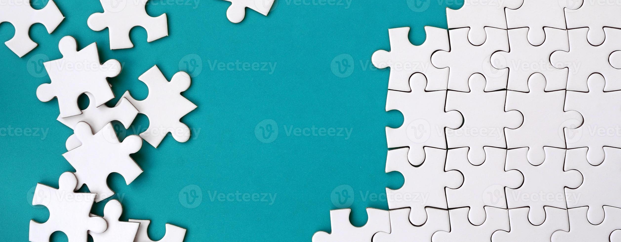 Fragment of a folded white jigsaw puzzle and a pile of uncombed puzzle elements against the background of a blue surface. Texture photo with space for text