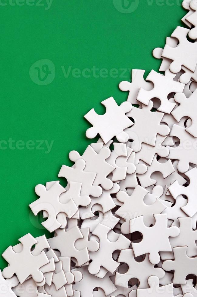 A pile of uncombed elements of a white jigsaw puzzle lies on the background of a green surface. Texture photo with copy space for text