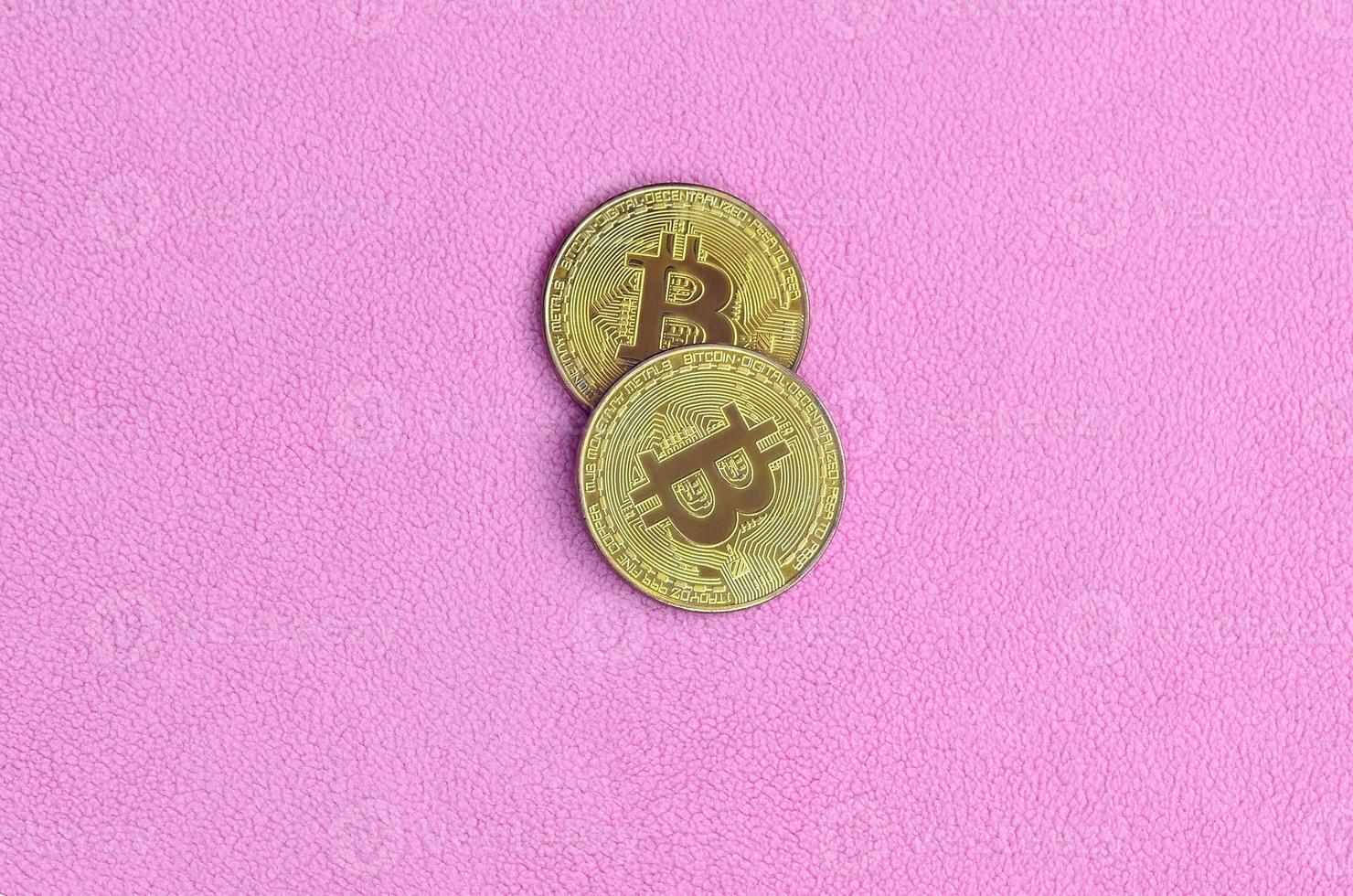 Two golden bitcoins lies on a blanket made of soft and fluffy light pink fleece fabric. Physical visualization of virtual crypto currency photo