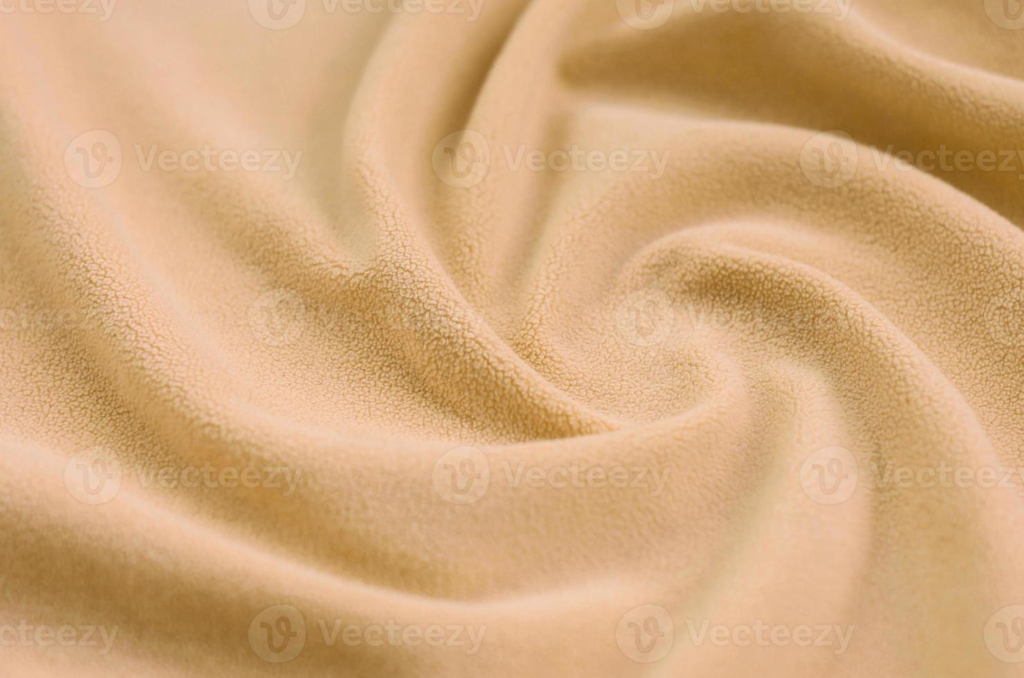 The blanket of furry orange fleece fabric. A background of light orange soft plush fleece material with a lot of relief folds photo