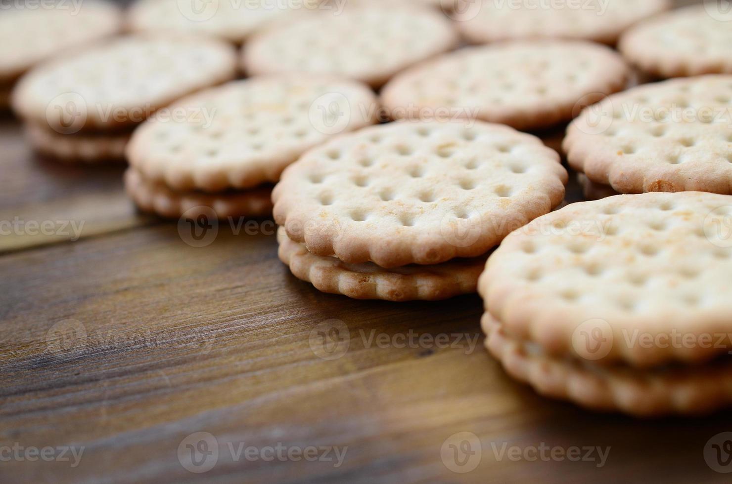 A round sandwich cookie with coconut filling lies in large quantities on a brown wooden surface. Photo of edible treats on a wooden background with copy space
