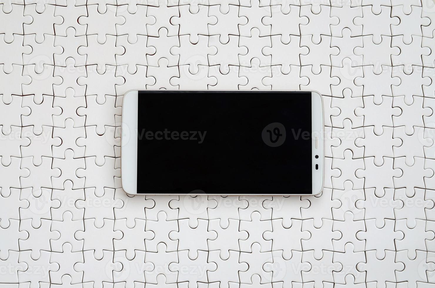 A modern big smartphone with a touch screen lies on a white jigsaw puzzle in an assembled state photo