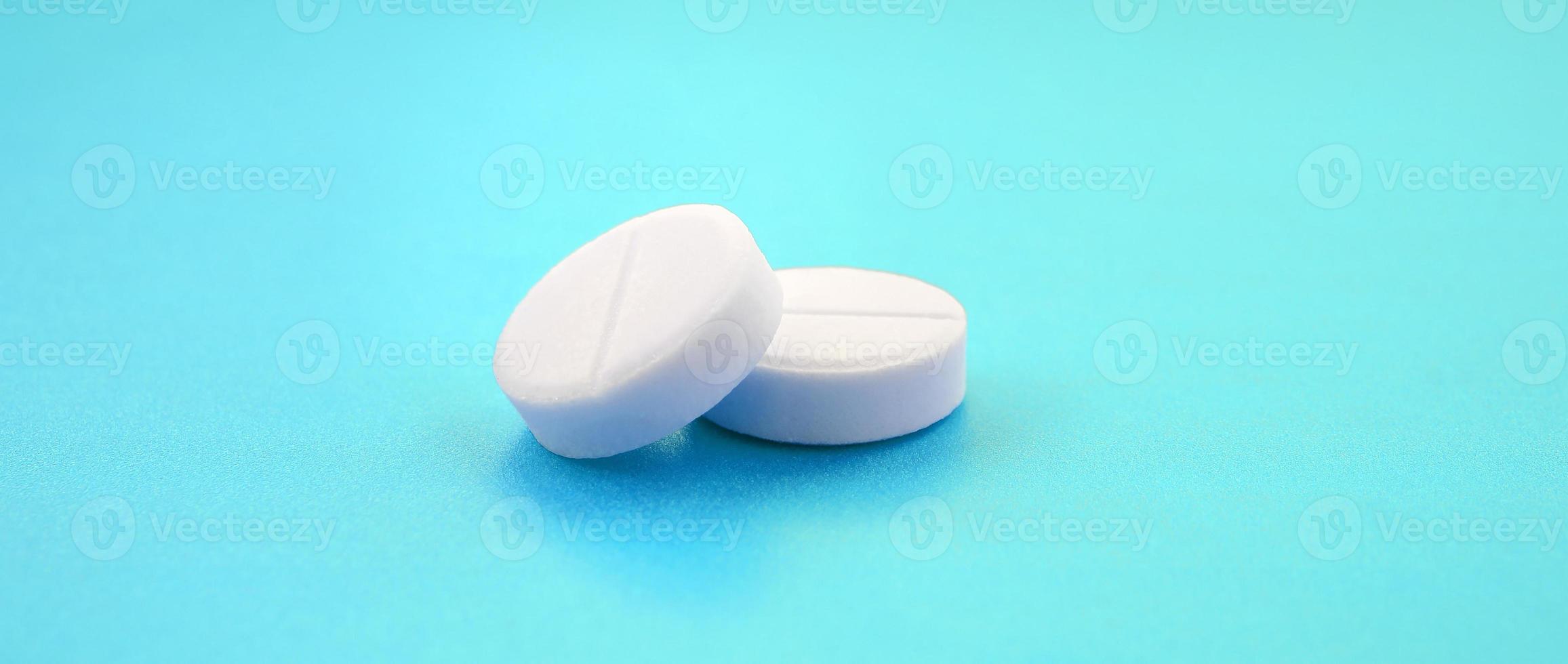 A few white tablets lie on a bright blue background surface. Background image on medical and pharmaceutical topics photo