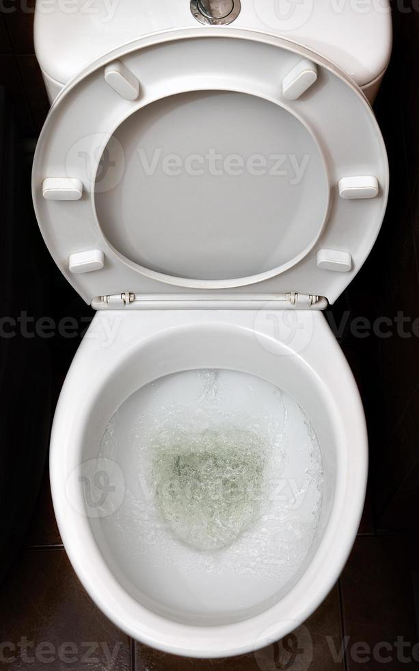 A photo of a white ceramic toilet bowl in the process of washing it off. Ceramic sanitary ware for correcting the need with an automatic flushing device
