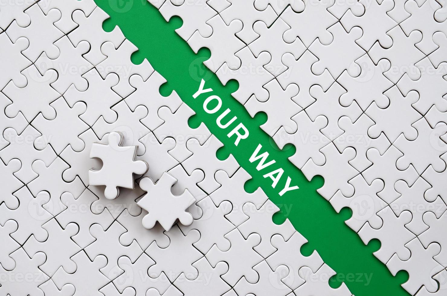 Your way. The green path is laid on the platform of a white folded jigsaw puzzle. The missing elements of the puzzle are stacked nearby photo