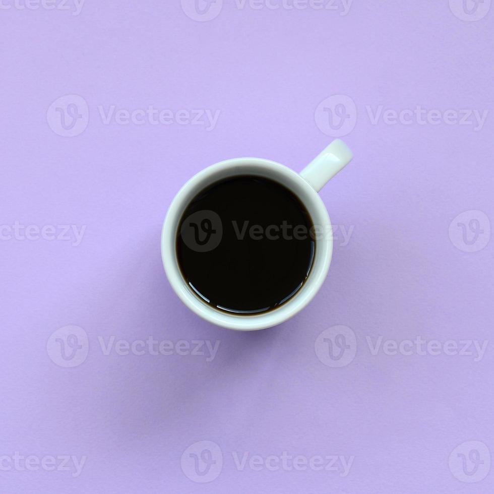 pequeña taza de café blanca sobre fondo de textura de papel de color violeta pastel de moda en concepto mínimo foto