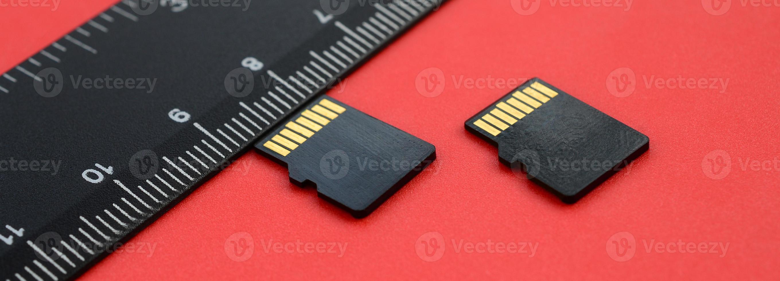 Two small micro SD memory cards lie on a red background next to a black ruler. A small and compact data and information store photo