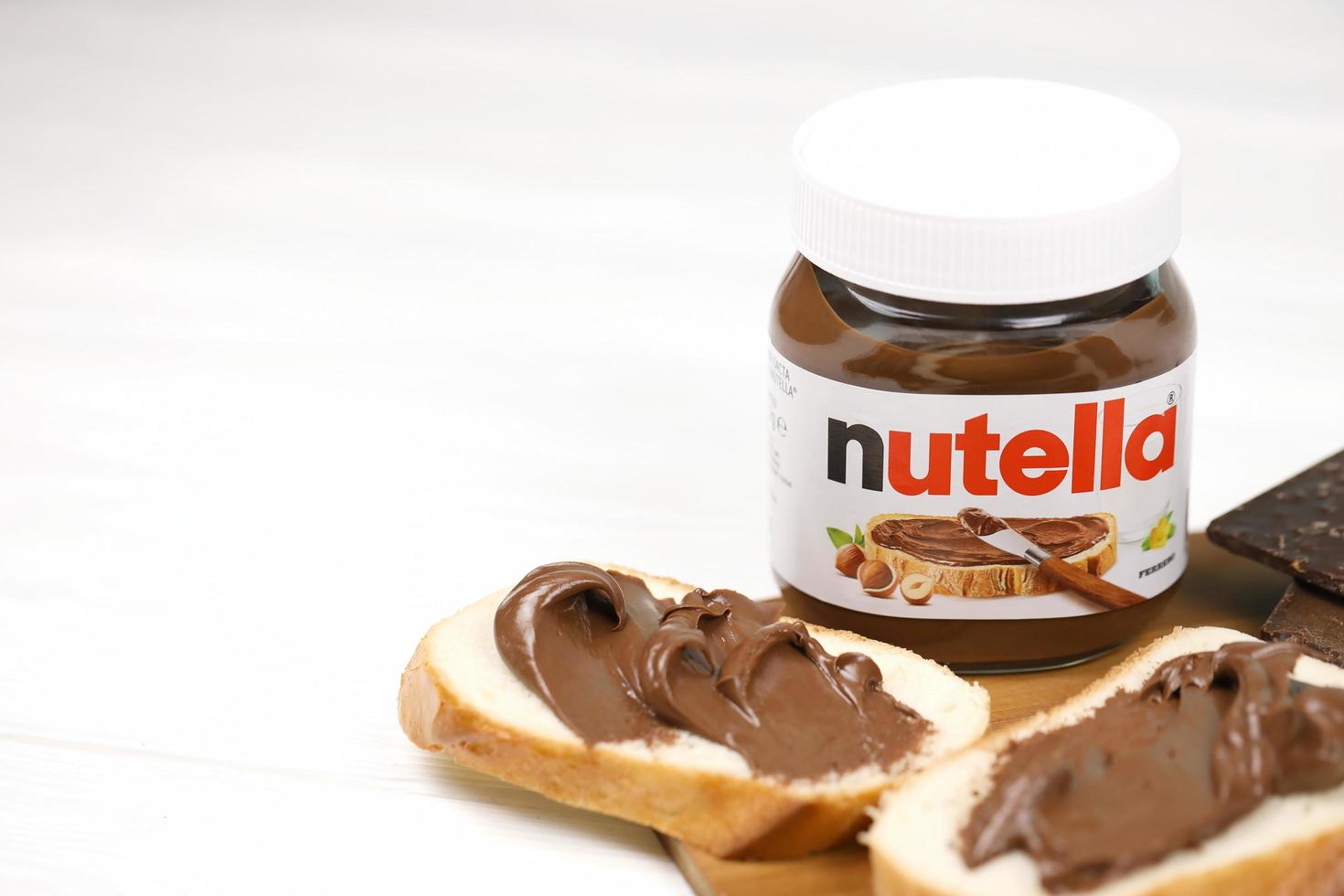 KHARKOV, UKRAINE - DECEMBER 27, 2020 Nutella glass can and spread on freshly baked bread. Nutella is manufactured by Italian company Ferrero first introduced in 1964 photo