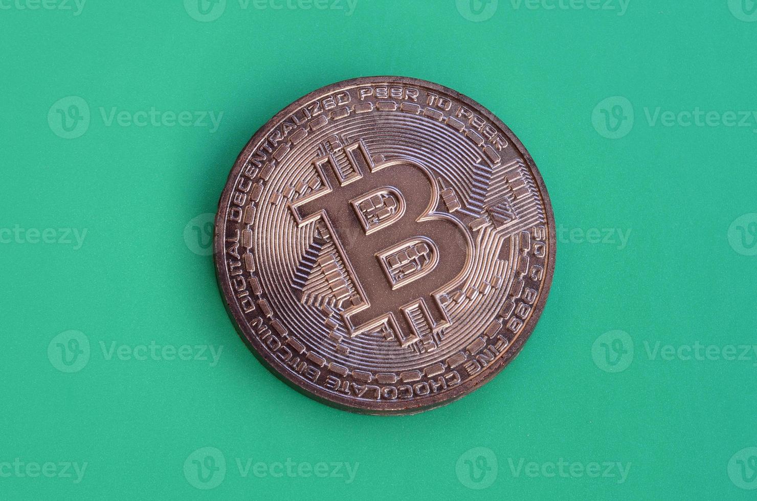 Chocolate product in the form of physical bitcoin lies on a green plastic background. Model of the crypto currency in the edible form photo
