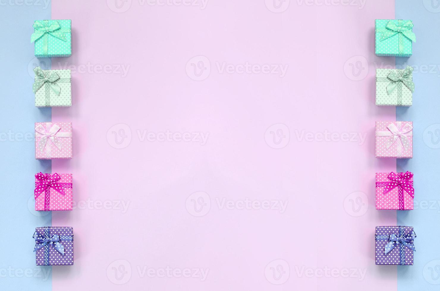 Small gift boxes of different colors with ribbons lies on a violet and pink background photo