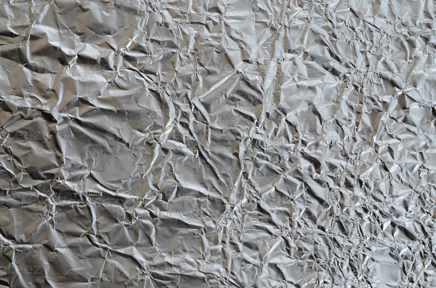 Thin wrinkled sheet of crushed tin aluminum silver foil background with shiny crumpled surface for texture photo