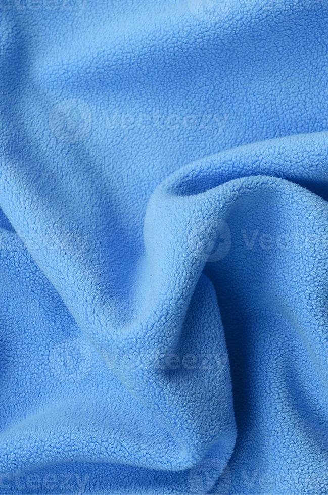 The blanket of furry blue fleece fabric. A background of light blue soft plush fleece material with a lot of relief folds photo