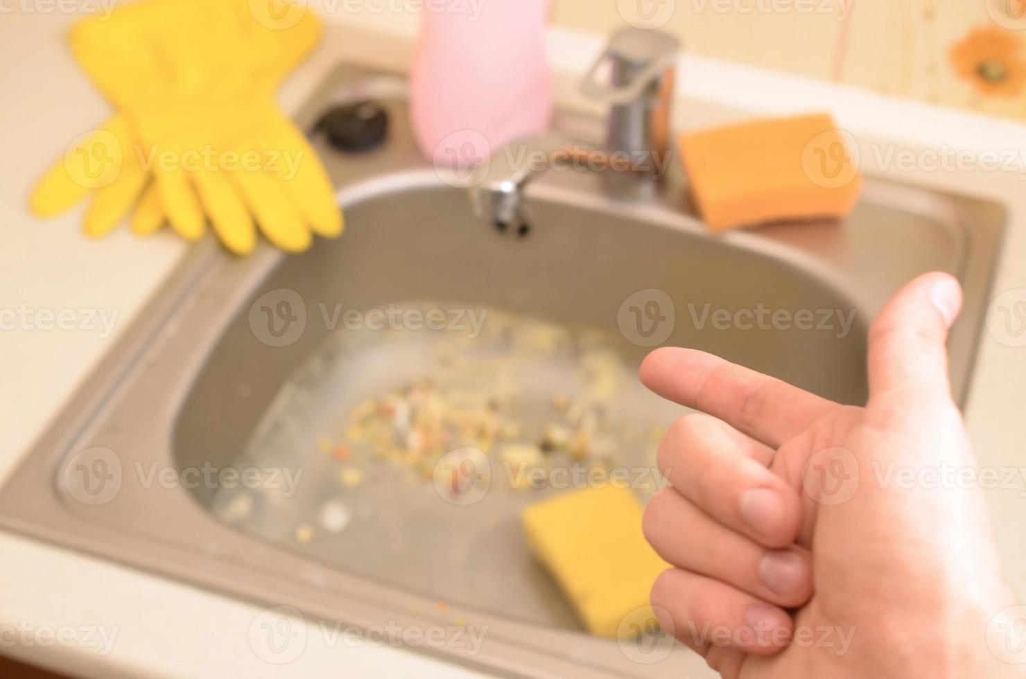 Hand points to dirty kitchen sink with many food particles before the cleaning photo