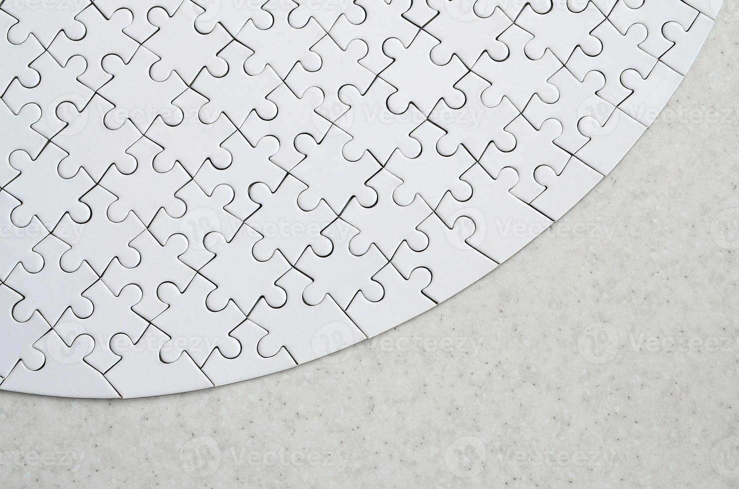 A white jigsaw puzzle in the complete form lies on a treated stone surface. Textured image with copy space photo