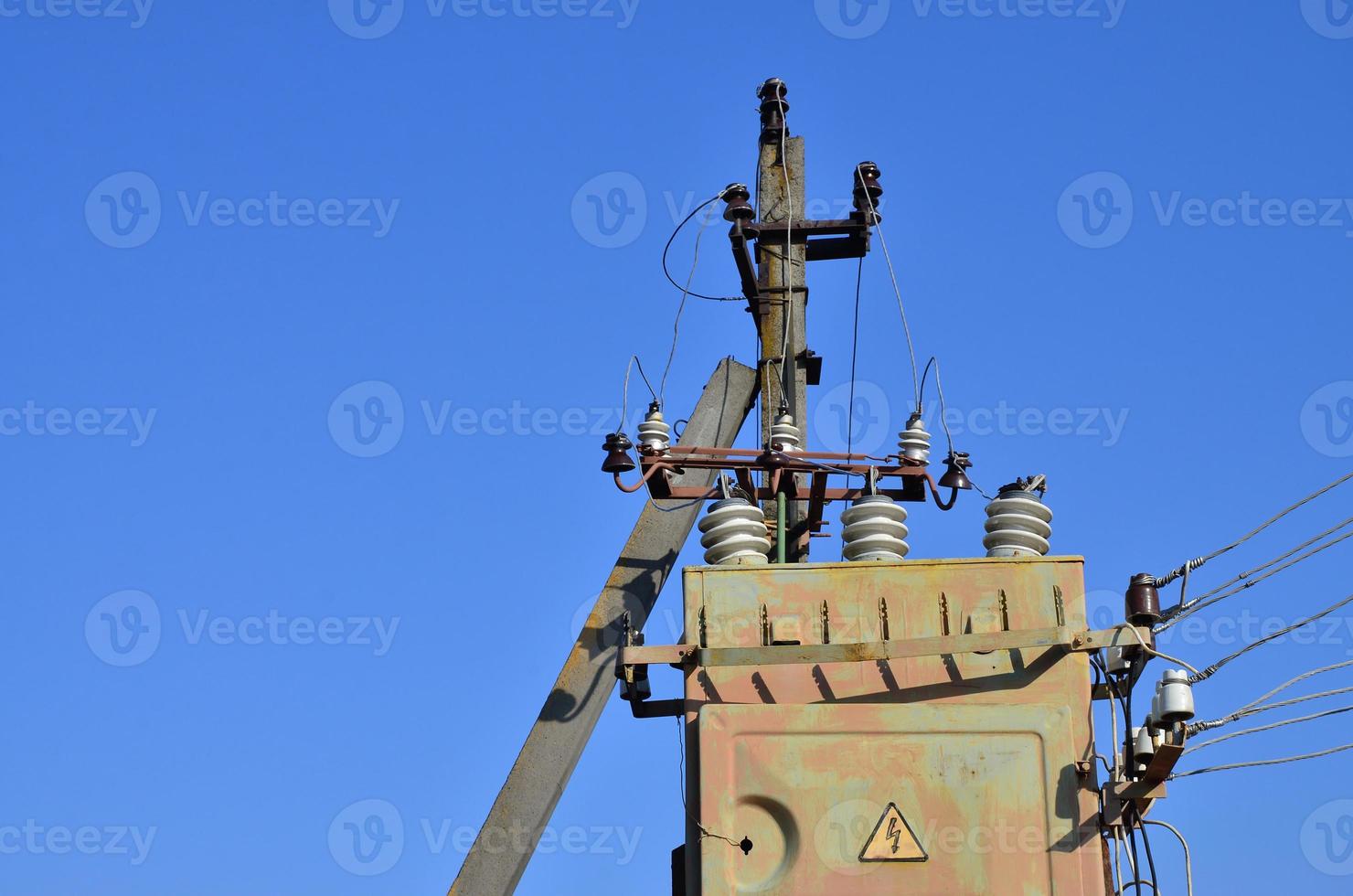 Old and obsolete electrical transformer against the background of a cloudless blue sky. Device for distribution of supply of high-voltage energy photo