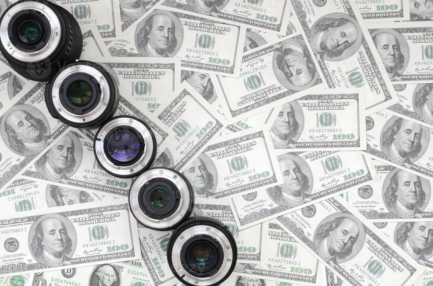 A few photographic lenses lies on the background of a lot of dollar bills. Space for text photo