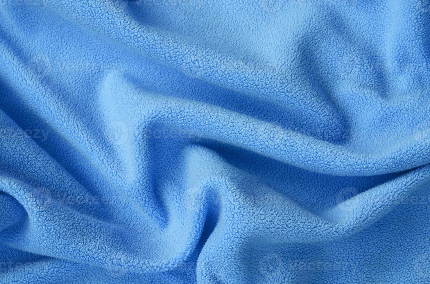 The blanket of furry blue fleece fabric. A background of light blue soft plush fleece material with a lot of relief folds photo