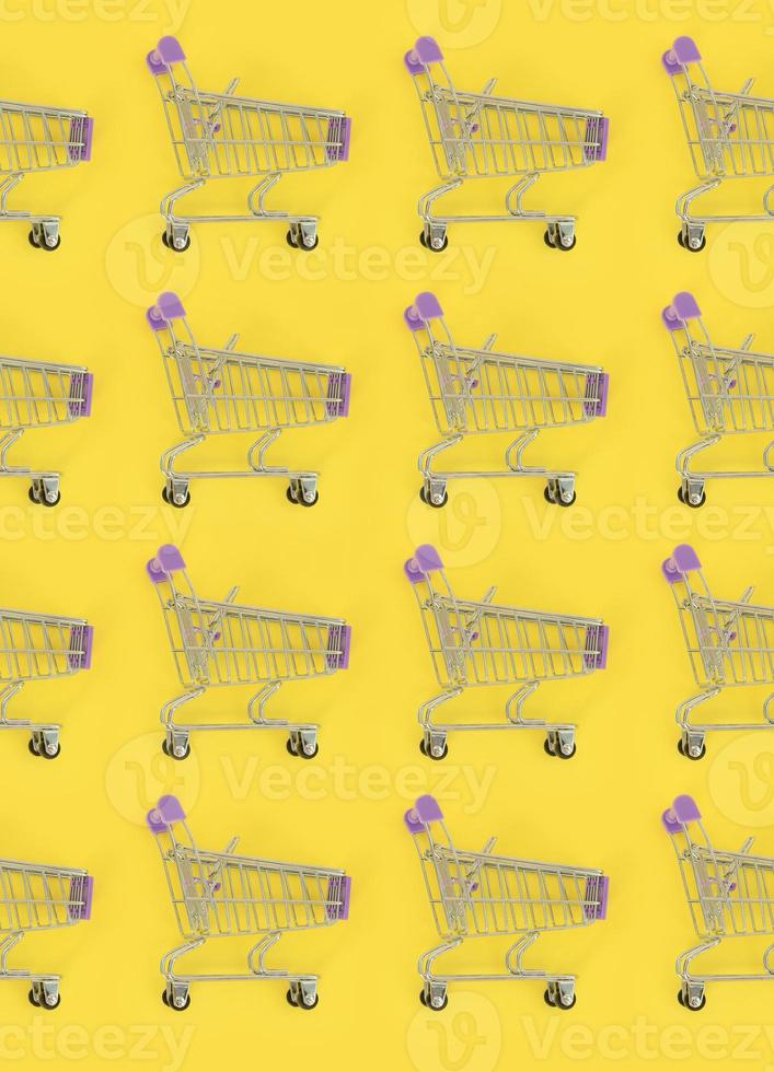 Shopping addiction, shopping lover or shopaholic concept. Many small empty shopping carts perform a pattern on a pastel colored paper background. Flat lay composition, top view photo
