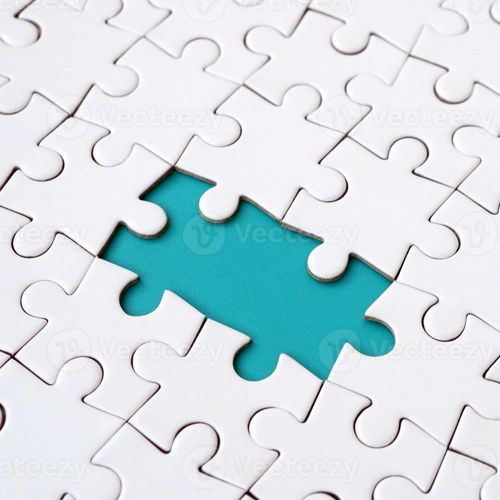 Close-up texture of a white jigsaw puzzle in assembled state with missing elements forming a blue pad for text. Copy space photo