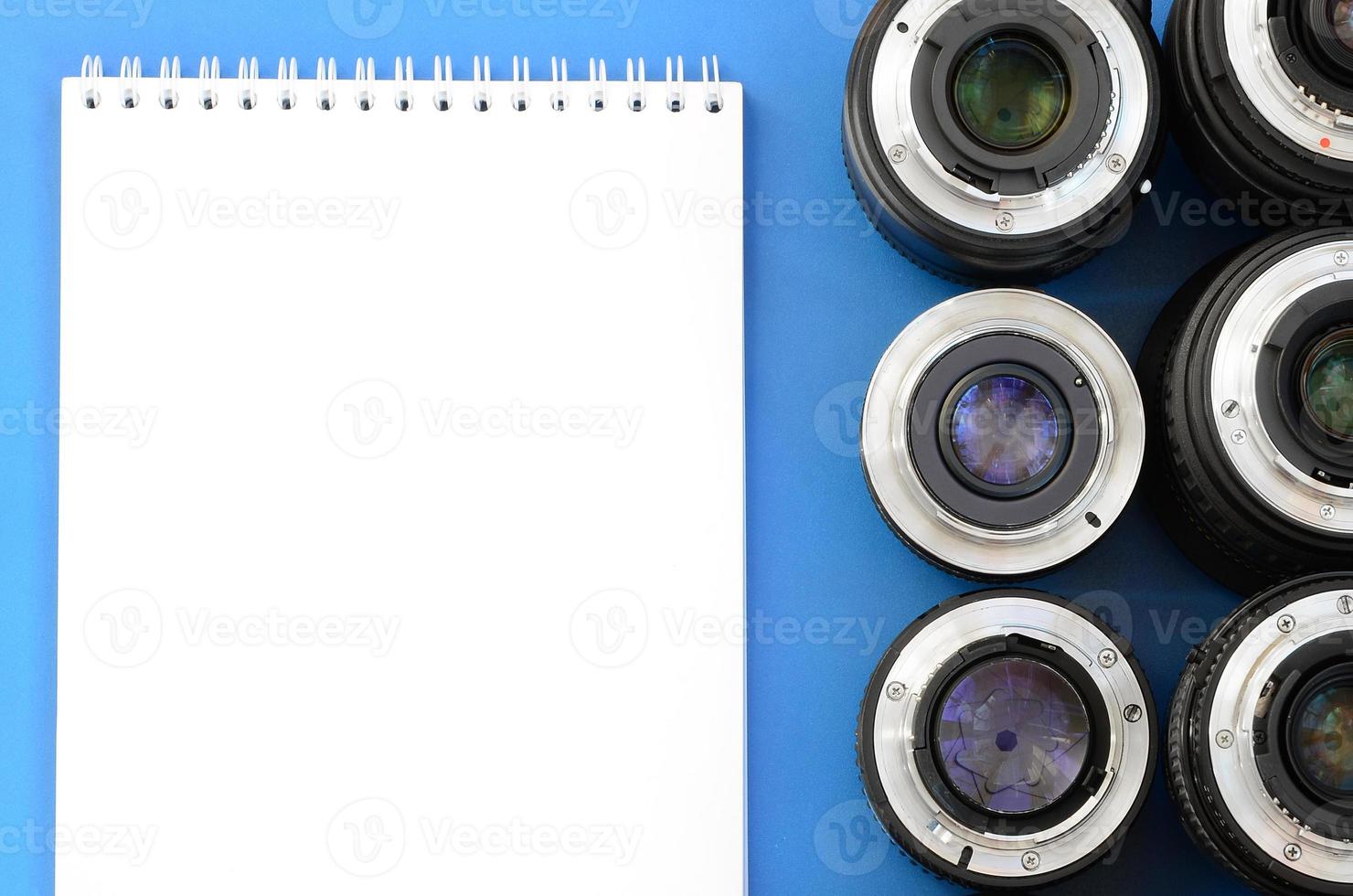 Several photographic lenses and white notebook lie on a bright blue background. Space for text photo